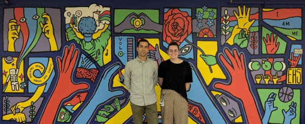 ASL interpreters, Ken Padilla (left) and Lexi Chiodo (right), standing in front of the deaf ed student mural